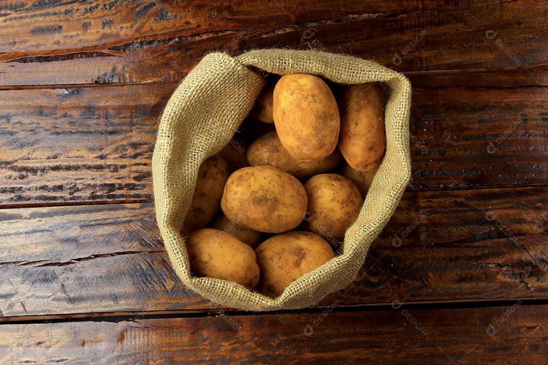 Batatas frescas e cruas colhidas da plantação e colocadas em um saco rústico na mesa de madeira