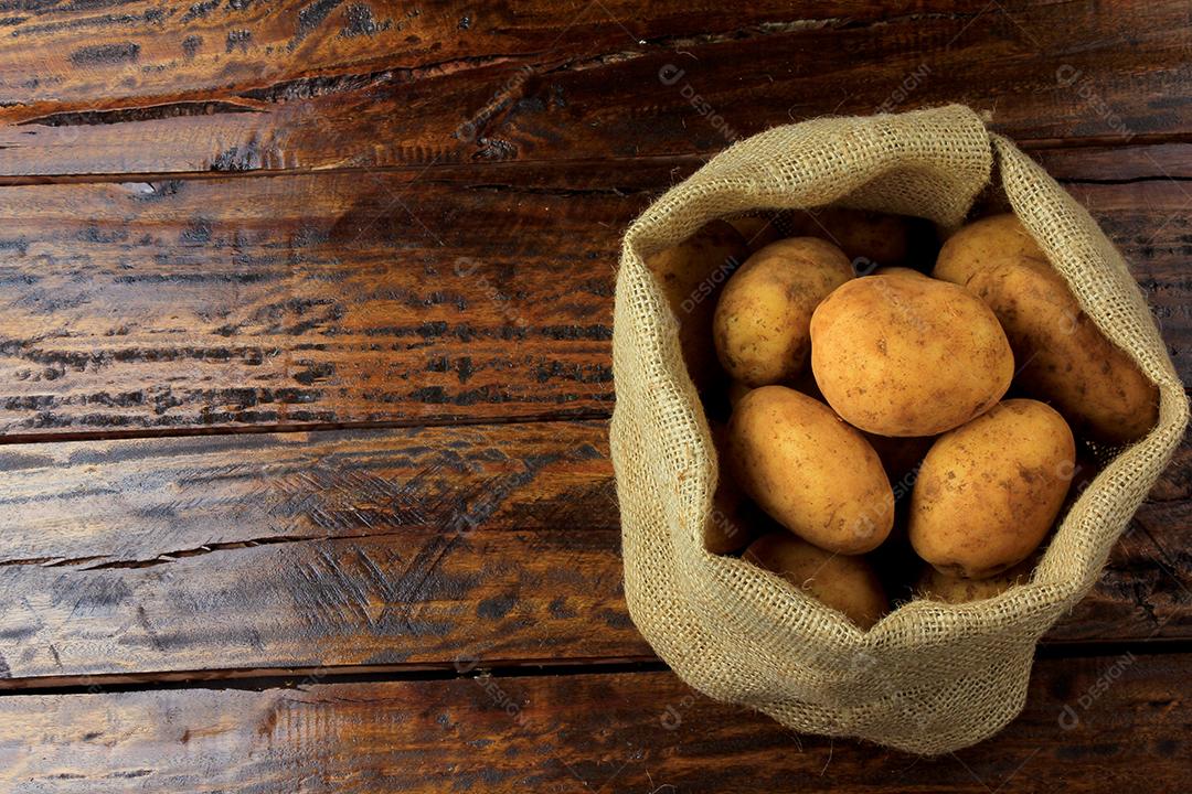 Batatas frescas e cruas colhidas da plantação e colocadas em um saco rústico na mesa de madeira