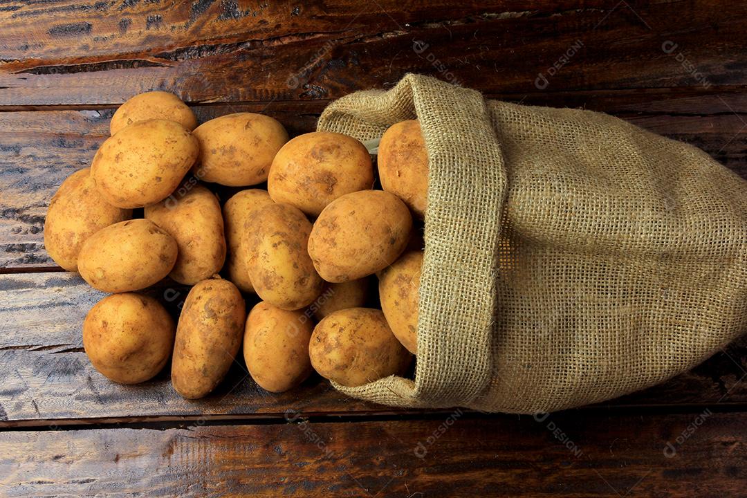 Batatas frescas e cruas colhidas da plantação e colocadas em um saco rústico na mesa de madeira