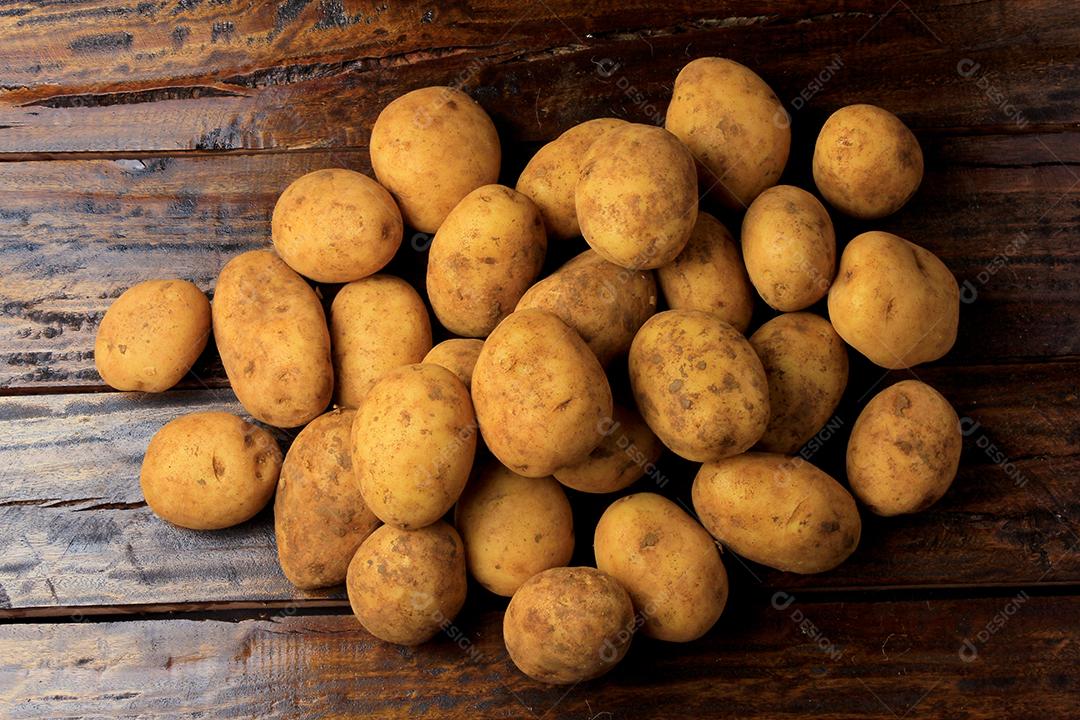 Batatas frescas e cruas colhidas da plantação e colocadas em um saco rústico na mesa de madeira