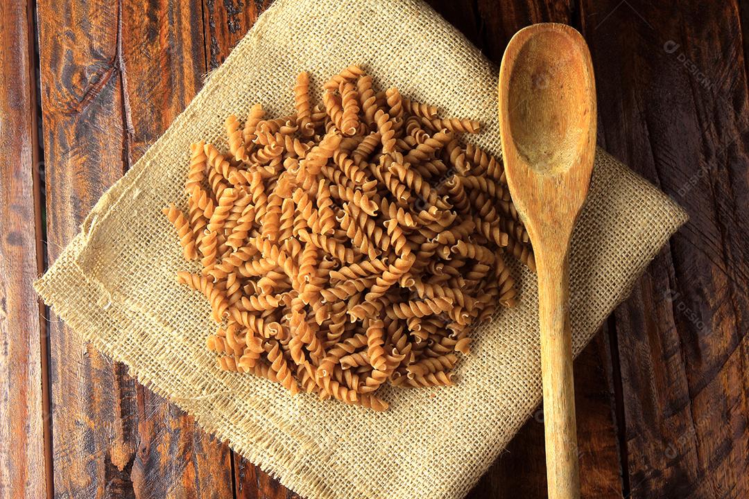 Vista superior de toda a massa de Fusilli em tecido toalha rústica com colher de pau sobre fundo de madeira