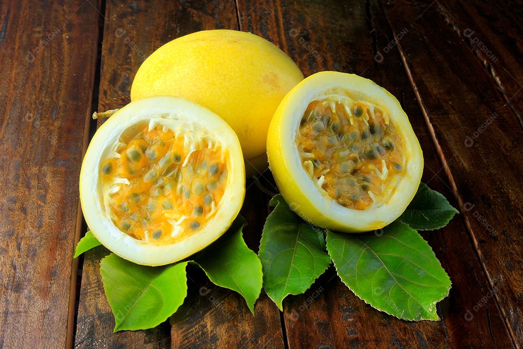 Maracujá amarelo e maracujá cortado ao meio em uma tigela de madeira na mesa de madeir