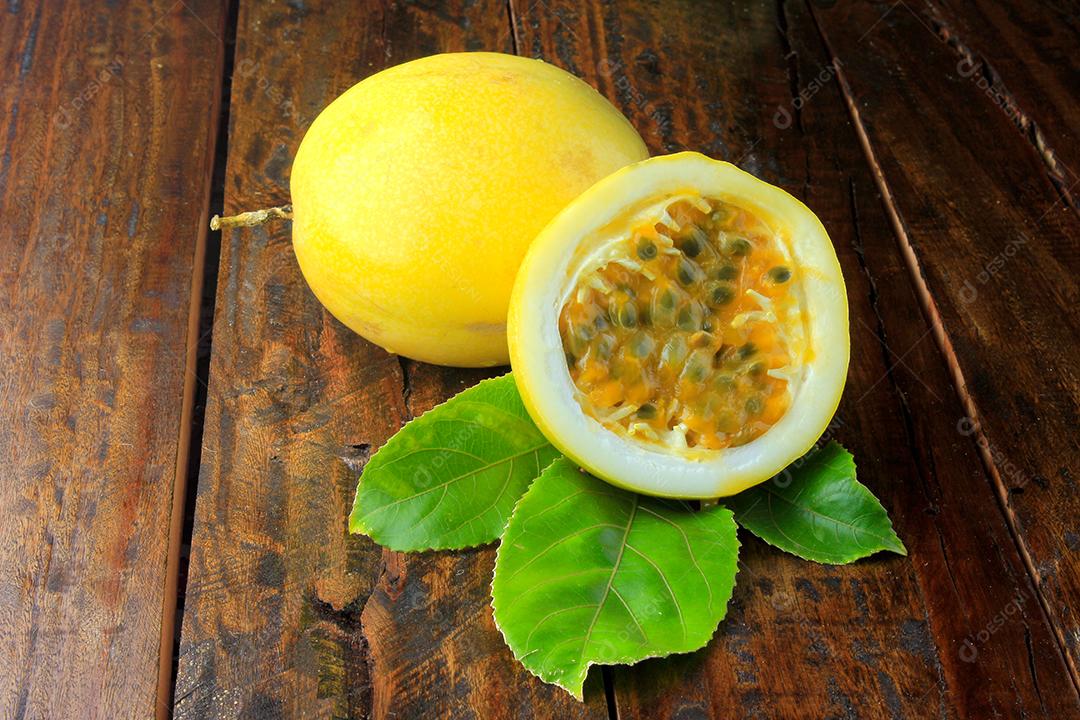 Maracujá amarelo e maracujá cortado ao meio em uma tigela de madeira na mesa de madeir