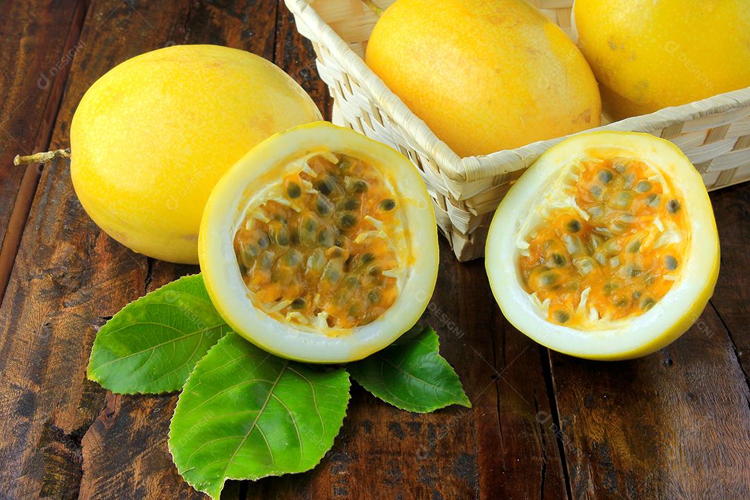 Maracujá amarelo e maracujá cortado ao meio em uma tigela de madeira na mesa de madeir