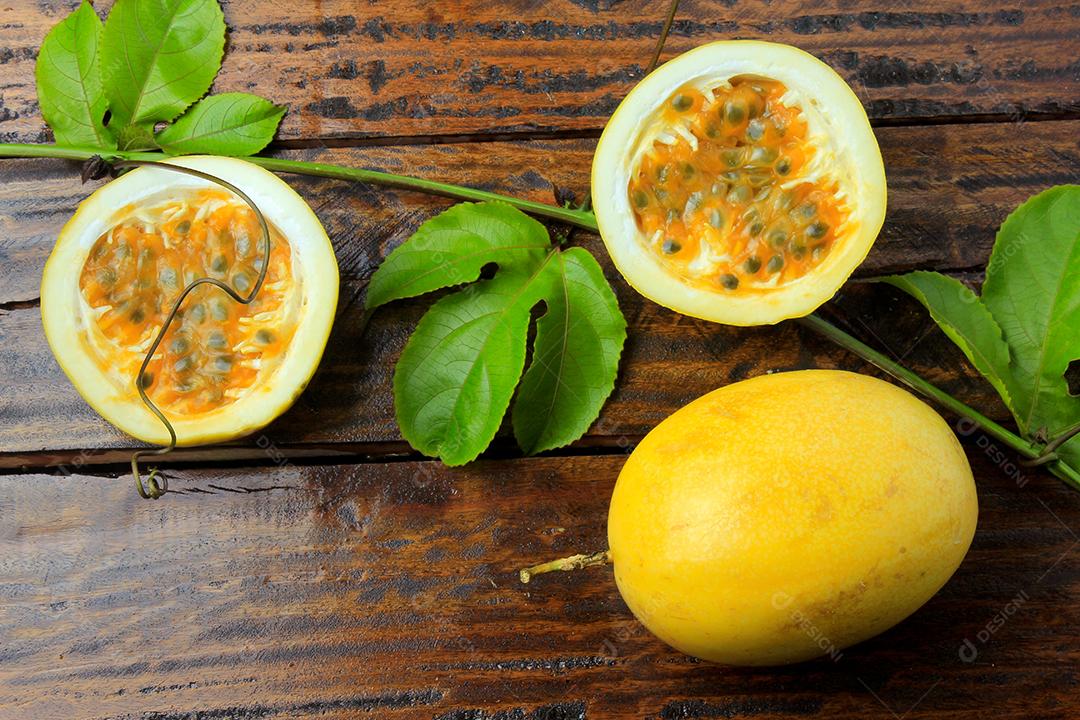 ramos e folhas com maracujá amarelo e maracujá cortado ao meio isolado na mesa de madeira. Vista do topo