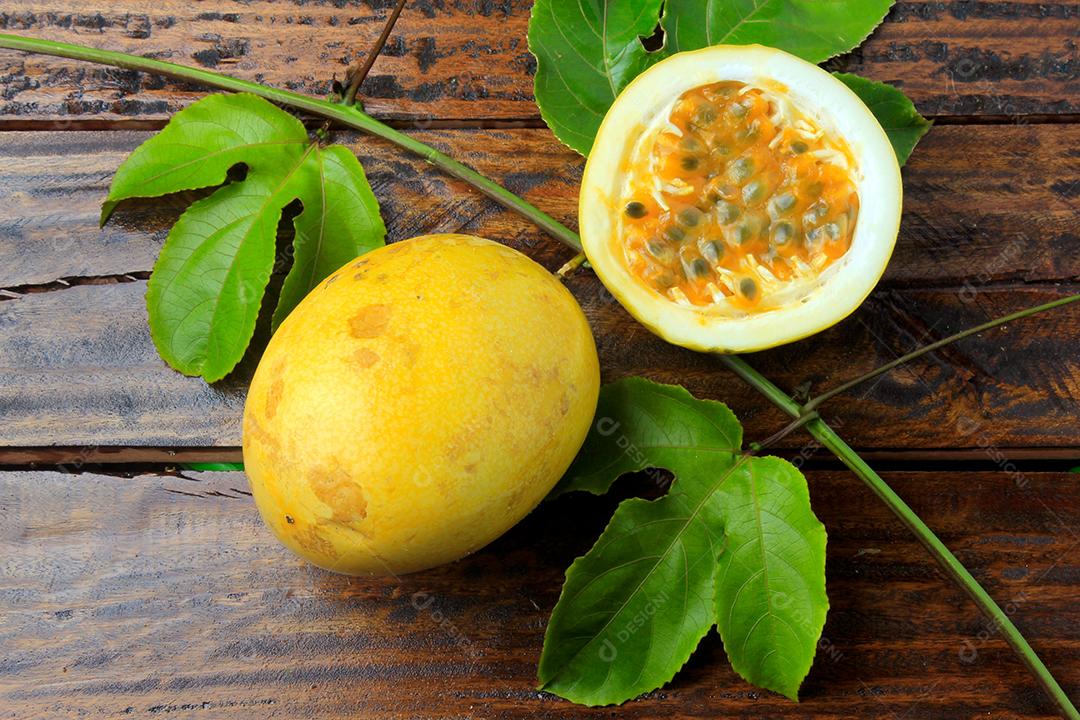 ramos e folhas com maracujá amarelo e maracujá cortado ao meio isolado na mesa de madeira. Vista superior de perto