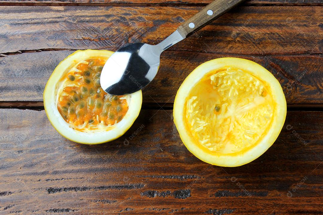 polpa de maracujá na colher de pau ao lado de maracujá inteiro com folha na mesa de madeira