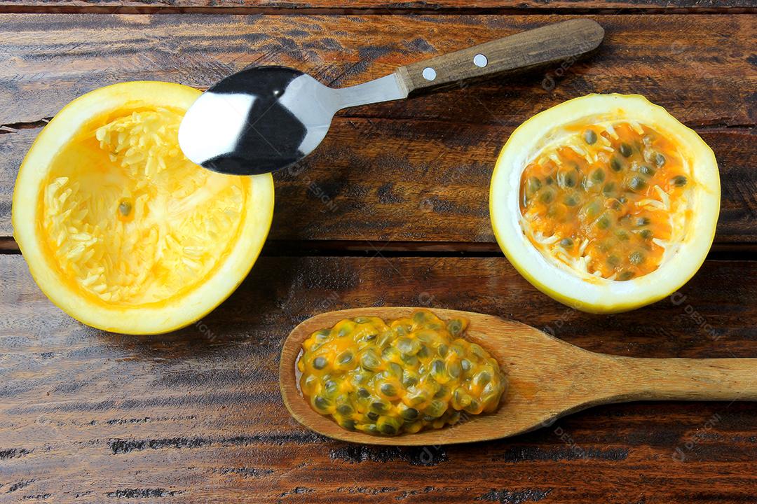 Colher de aço inoxidável, removendo a polpa de maracujá amarelo na mesa de madeira. Vista do topo