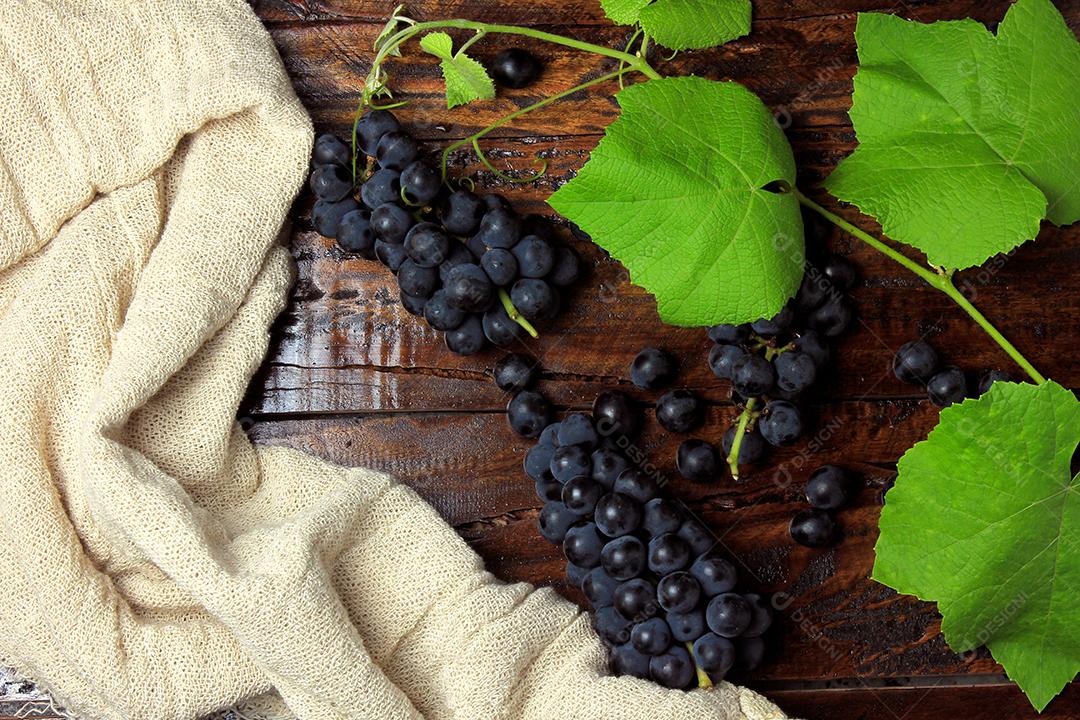 cachos de uvas frescas com galhos e folhas na mesa de madeira rústica