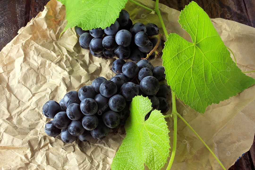 cachos de uvas frescas, com galhos e folhas, em papel, mesa de madeira rústica