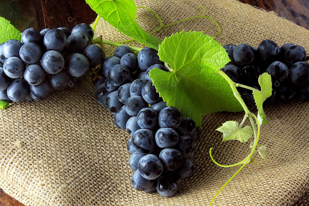cachos de uvas frescas com galhos e folhas na mesa de madeira rústica