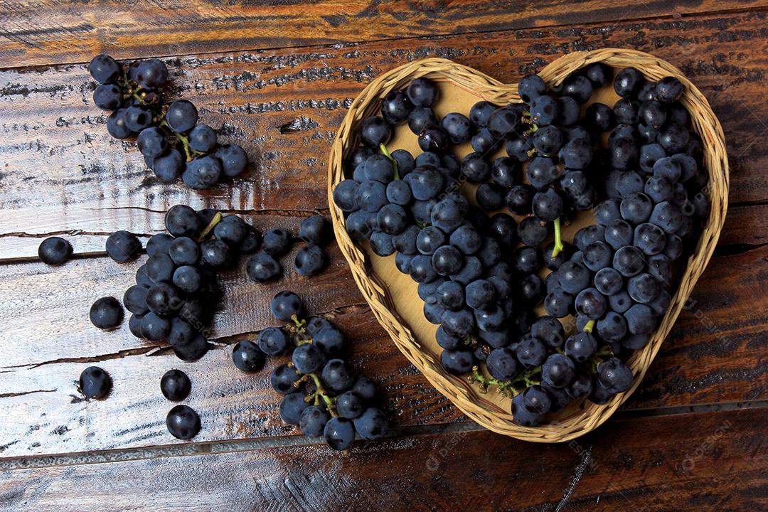 cachos de uva dentro da cesta com forma de coração na mesa de madeira, vista superior