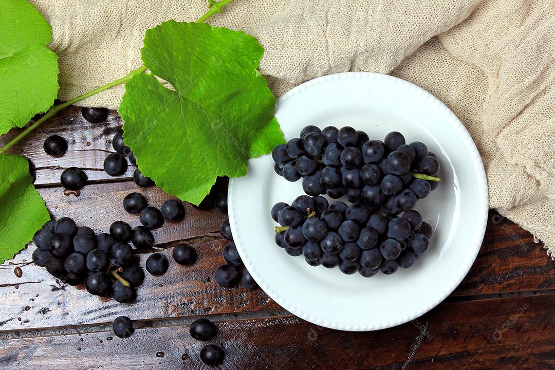 cachos de uvas frescas, dentro do prato cerâmico, na mesa de madeira rústica, vista superior