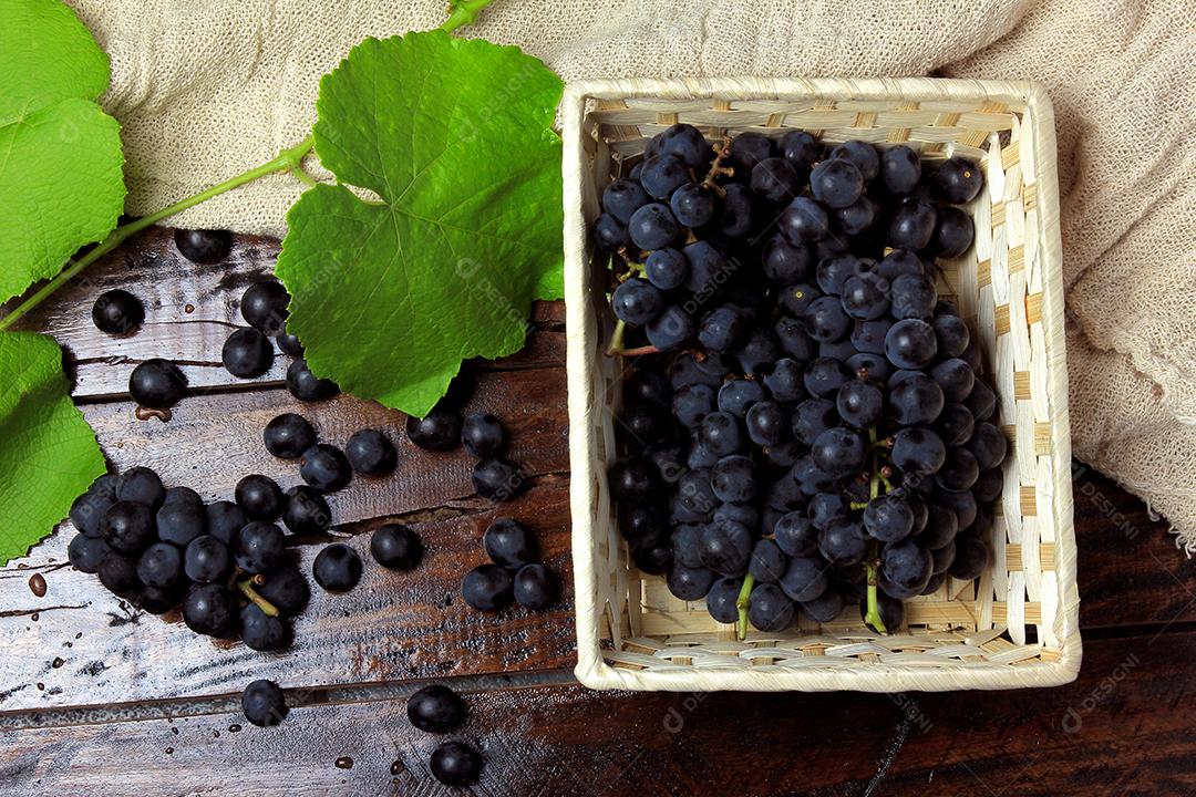 cachos de uvas frescas, dentro do prato cerâmico, na mesa de madeira rústica, vista superior