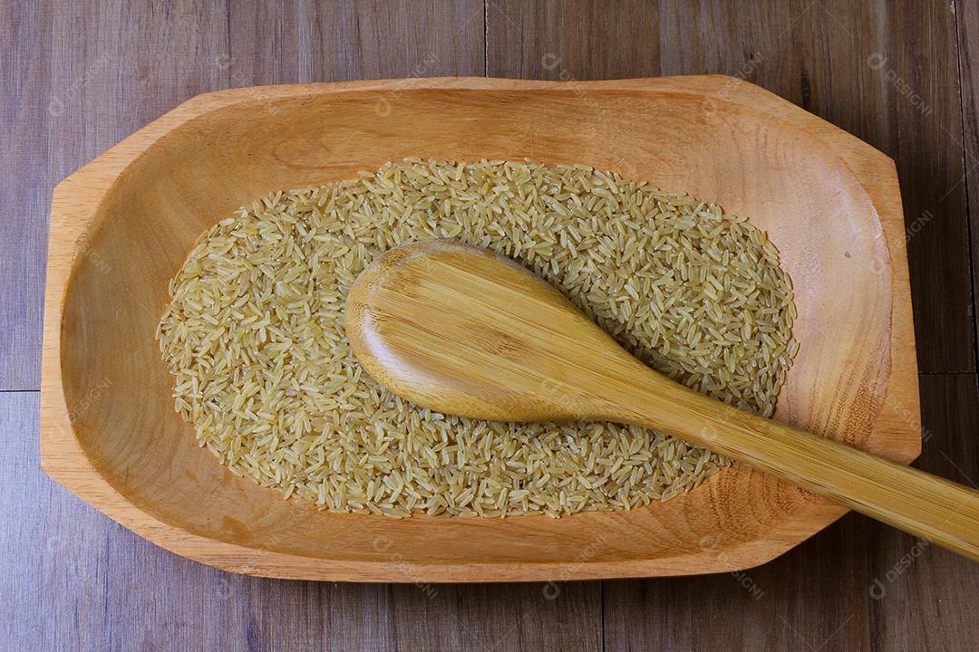 porção de arroz integral cru, tigela de madeira, mesa de madeira, vista superior