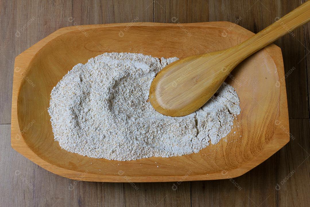 porção de farinha de trigo integral crua, tigela de madeira, mesa de madeira, vista superior