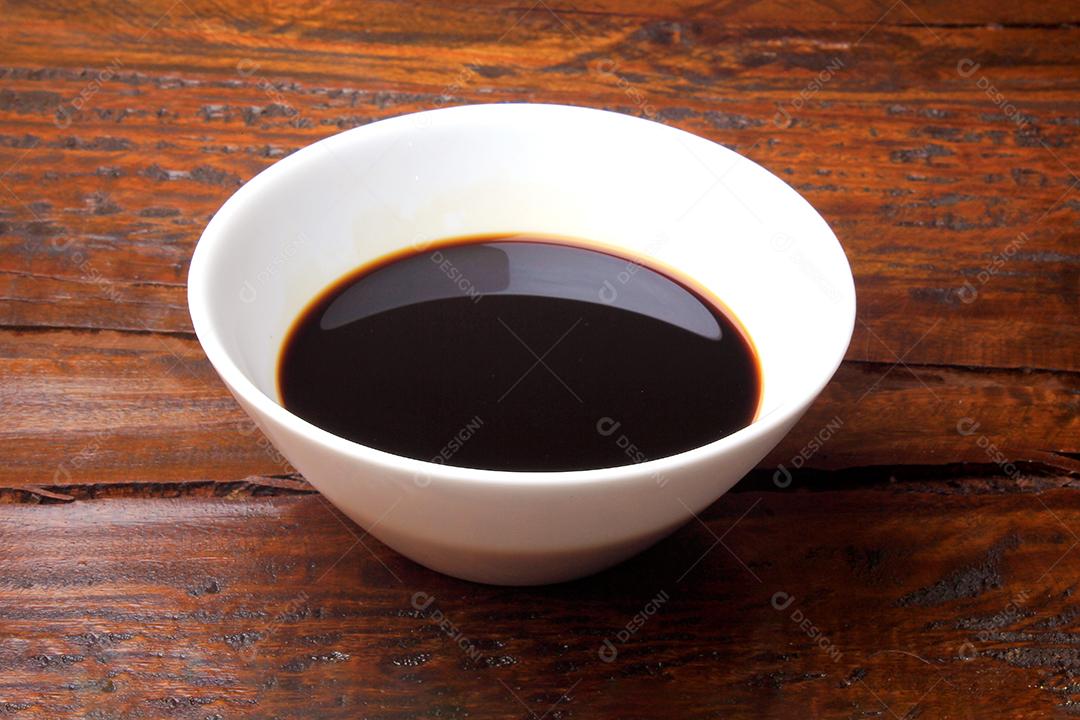 molho de soja escuro em uma tigela de cerâmica branca isolada na mesa de madeira rústica