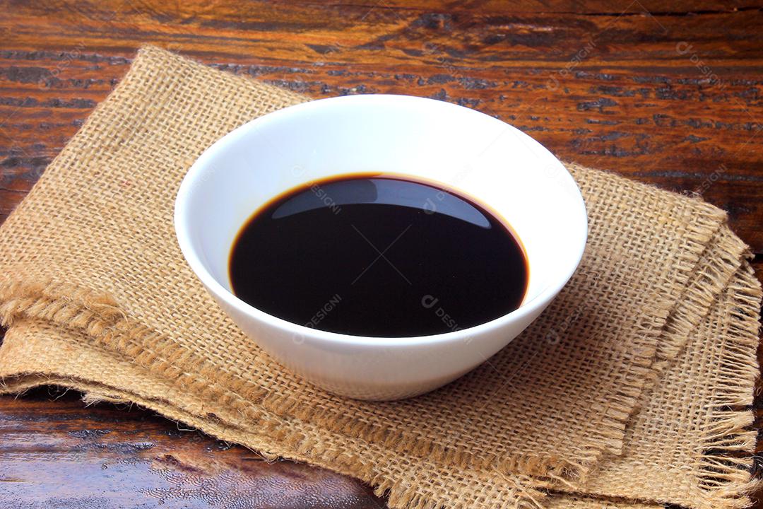 molho de soja escuro em uma tigela de cerâmica branca isolada na mesa de madeira rústica