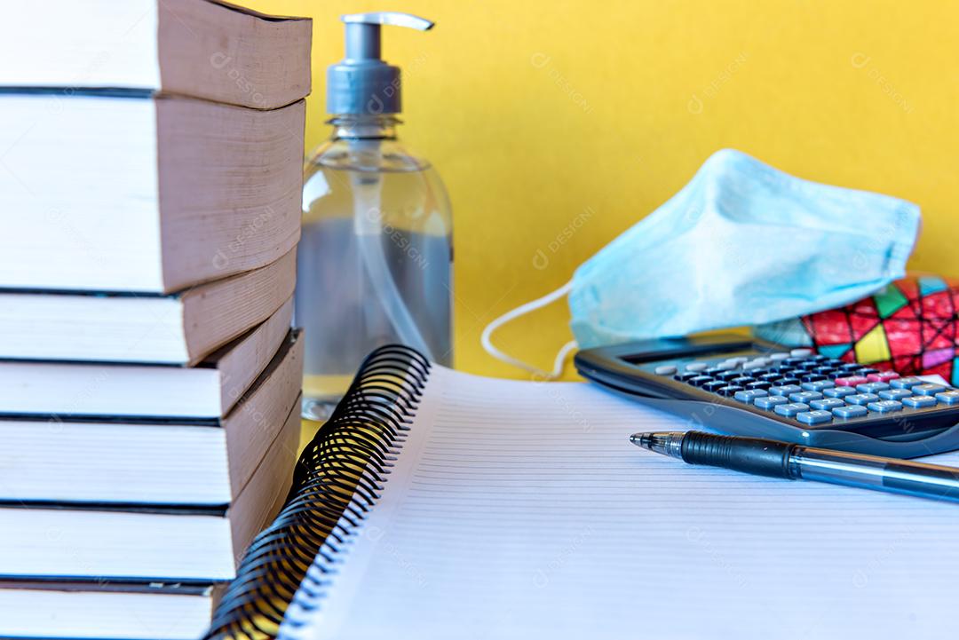 Mesa bagunçada com notebook, calculadora e livros. Educação, álcool gel e máscara, prevenção para Coronavirus