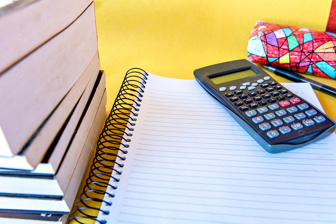 Mesa bagunçada com notebook, calculadora e livros.