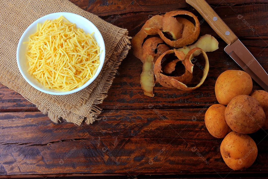 palitos de batata frita em tigela de cerâmica na mesa de madeira rústica com batatas cortadas. Vista do topo