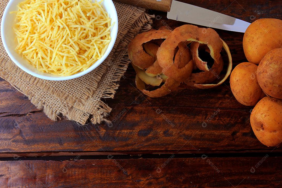 palitos de batata frita em tigela de cerâmica na mesa de madeira rústica com batatas cortadas. Vista do topo