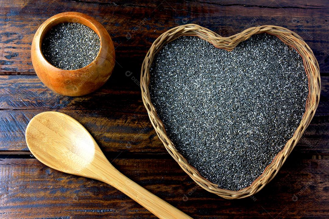 sementes de chia na cesta com forma de coração isolada na mesa rústica ao lado da colher. Vista do topo