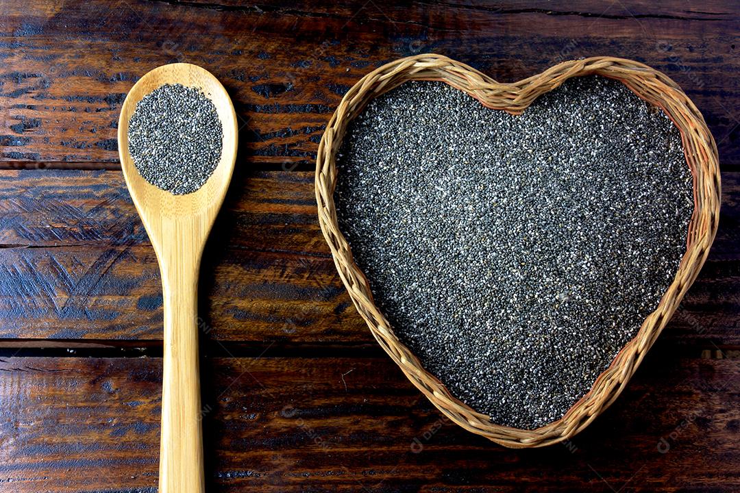 sementes de chia na cesta com forma de coração isolada na mesa rústica ao lado da colher. Vista do topo
