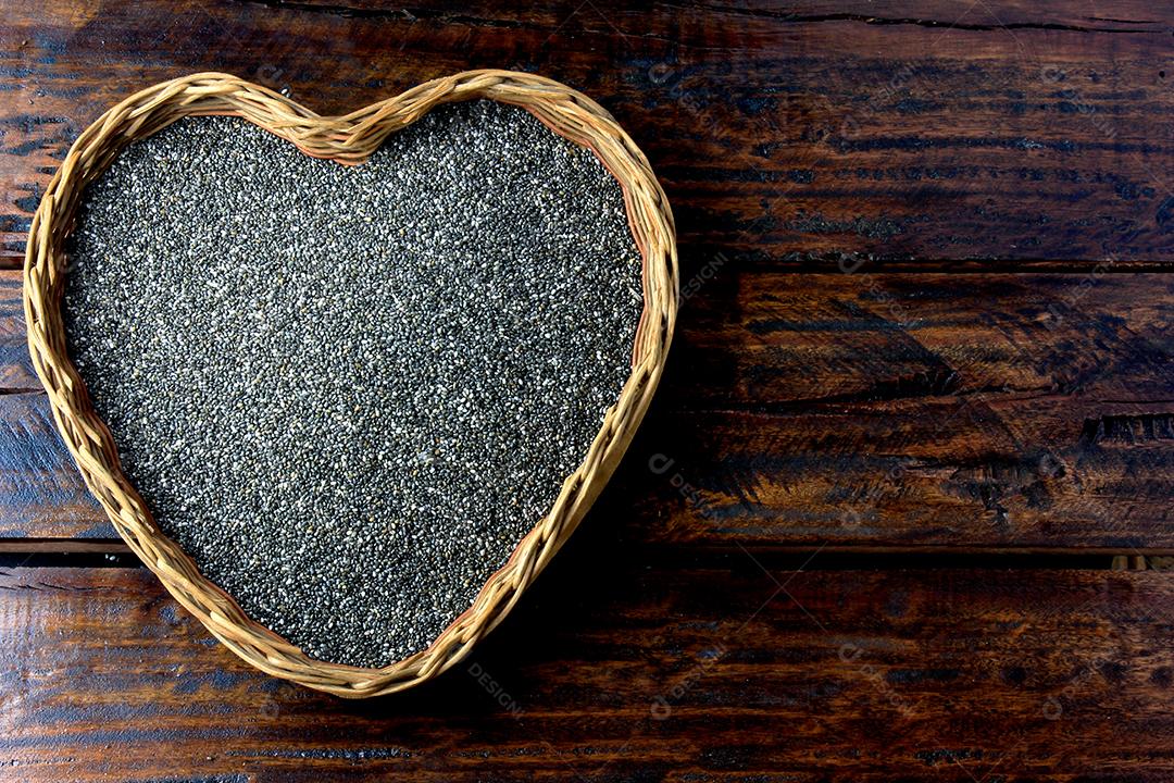 sementes de chia na cesta com forma de coração isolada na mesa rústica ao lado da colher. Vista do topo
