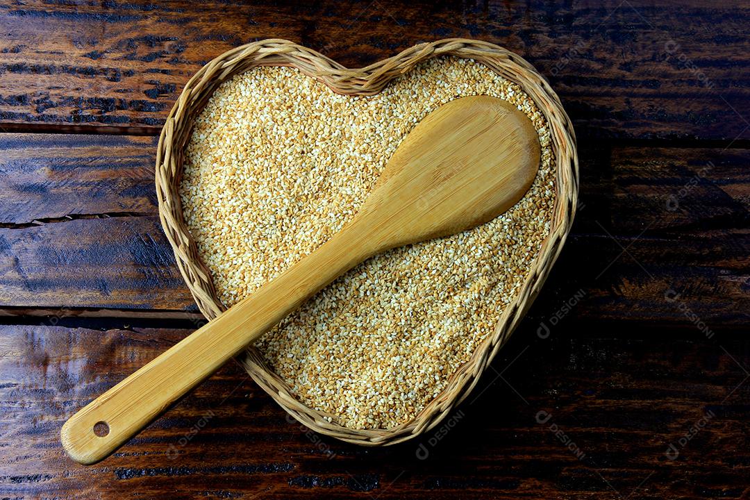 Sementes de gergelim na cesta com forma de coração isolada na mesa de madeira rústica, vista superior.