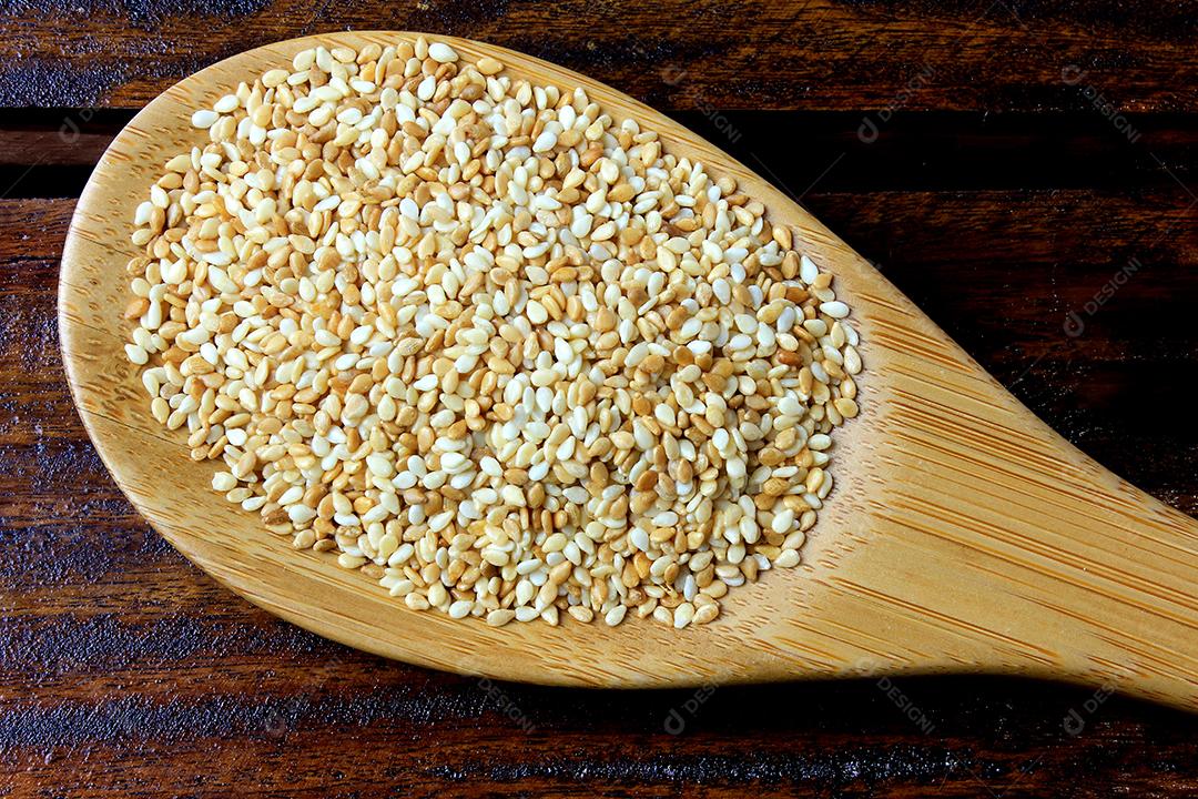 Sementes de gergelim na colher de bambu isoladas na mesa de madeira rústica, vista superior.