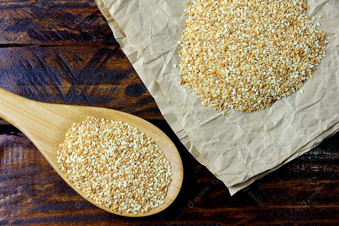 Sementes de gergelim na colher de bambu isoladas na mesa de madeira rústica, vista superior.