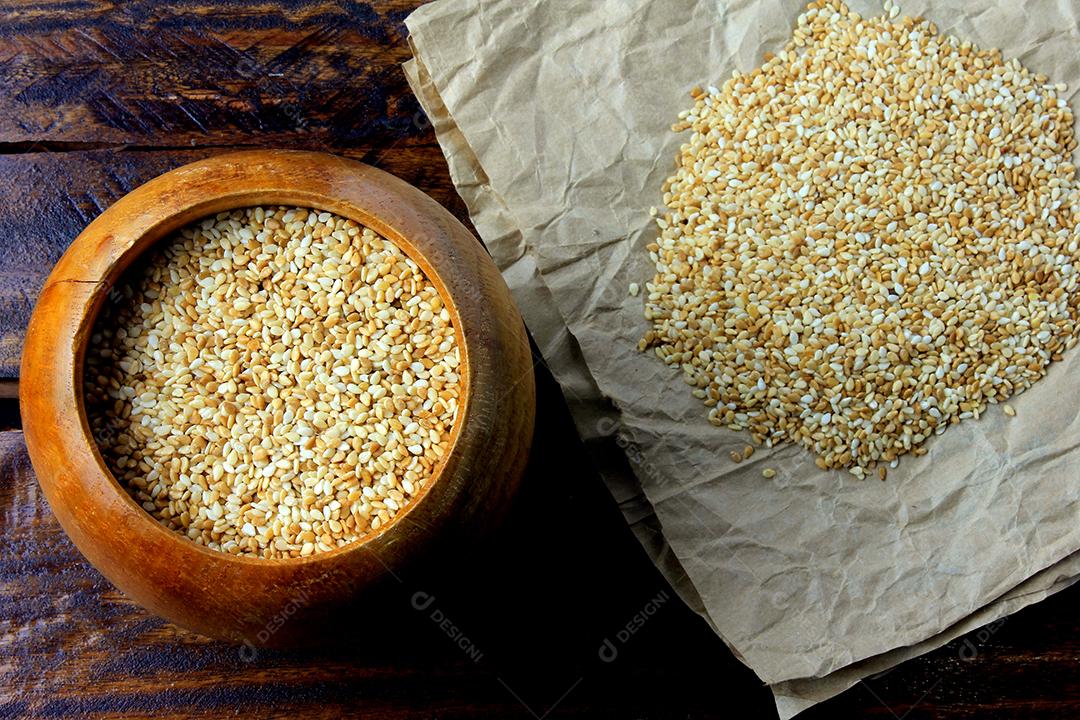 Sementes de gergelim em tigela de madeira isoladas na mesa de madeira rústica de fundo, vista superior.