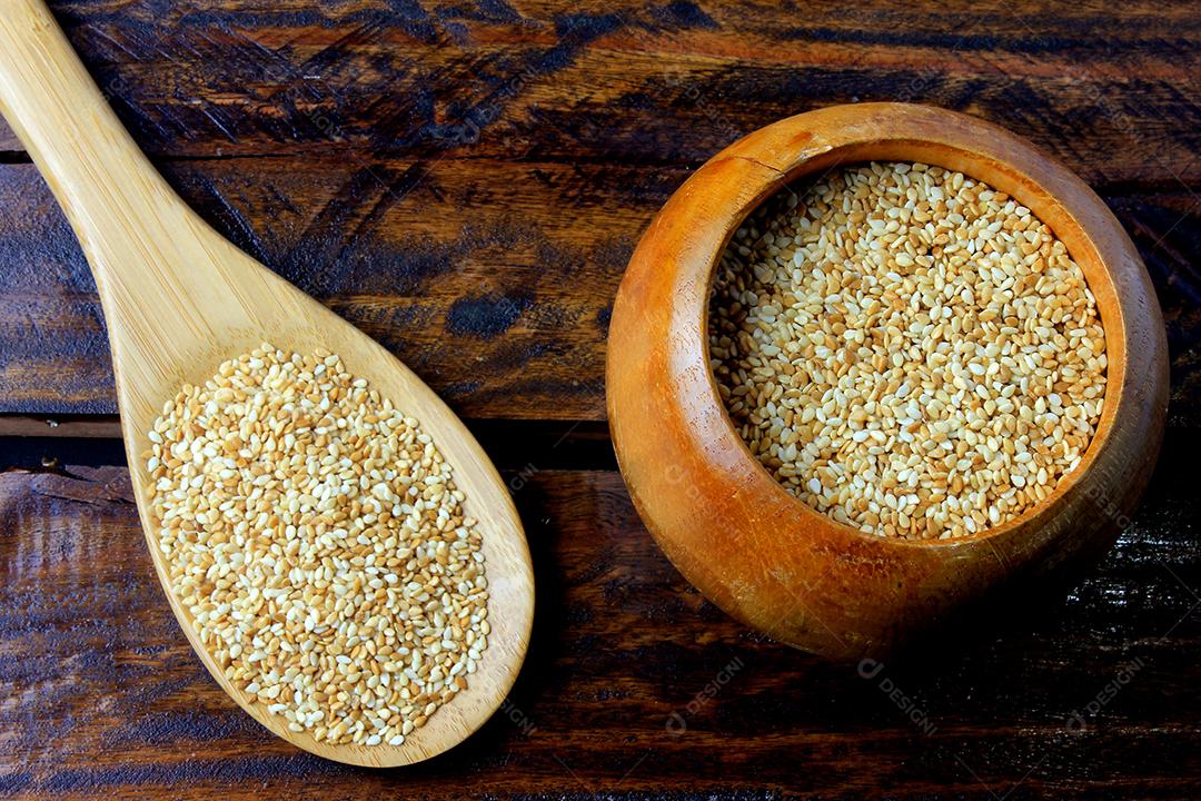Sementes de gergelim em tigela de madeira isoladas na mesa de madeira rústica de fundo, vista superior.