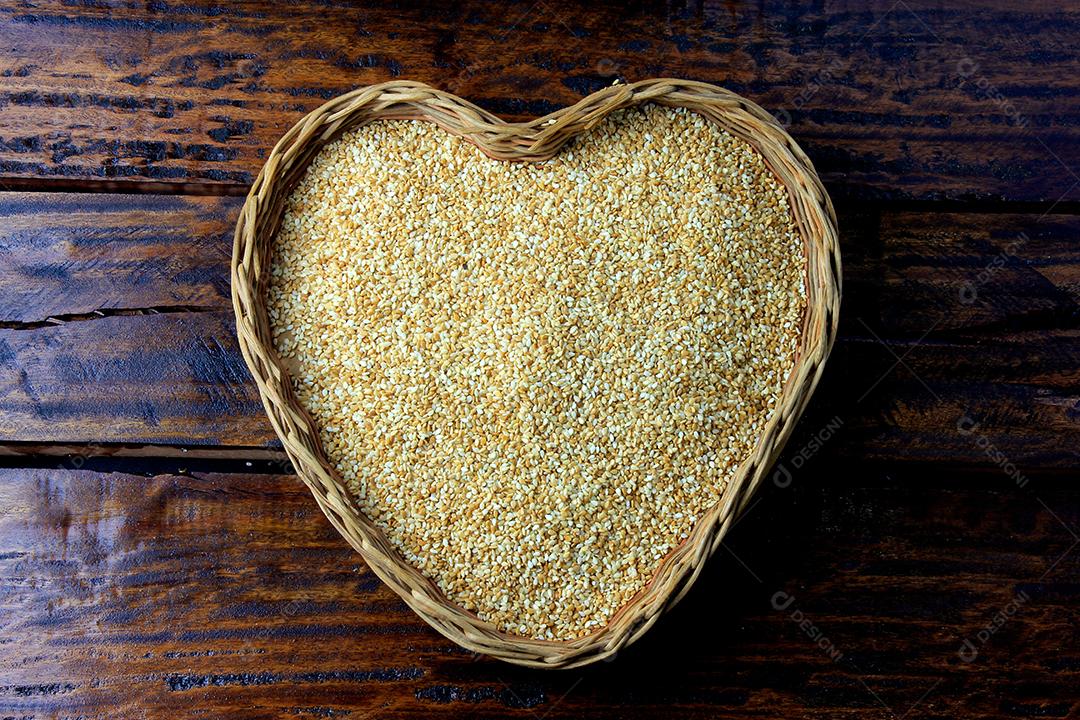 Sementes de gergelim na cesta com forma de coração isolada na mesa de madeira rústica, vista superior.