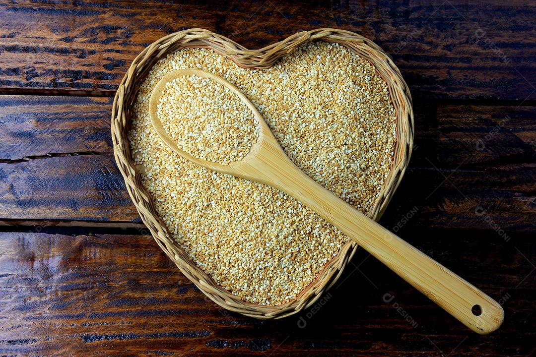 Sementes de gergelim na cesta com forma de coração isolada na mesa de madeira rústica, vista superior.