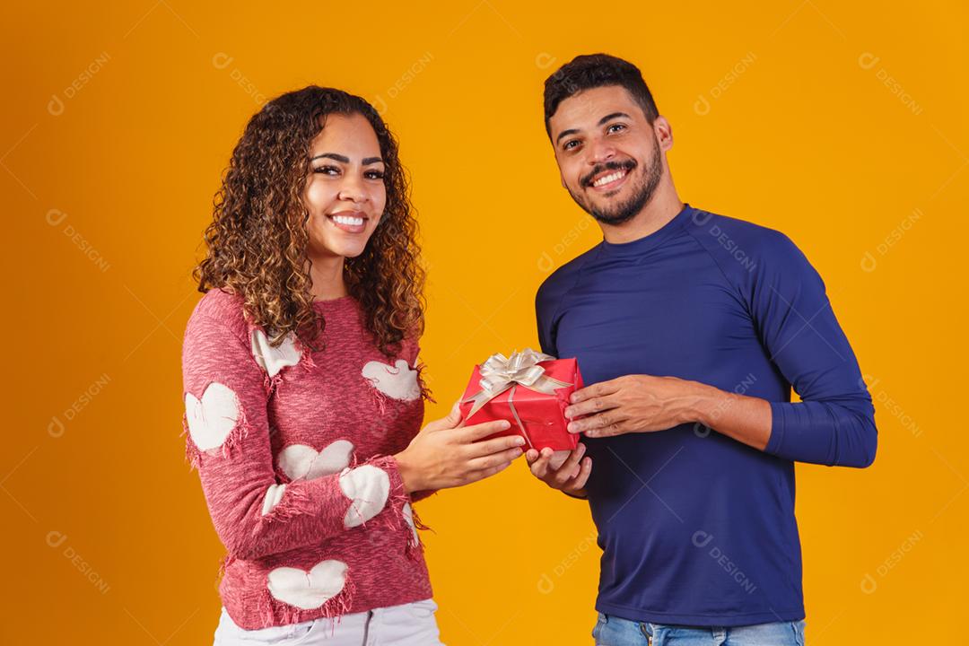 Retrato de um lindo casal em fundo amarelo com um presente