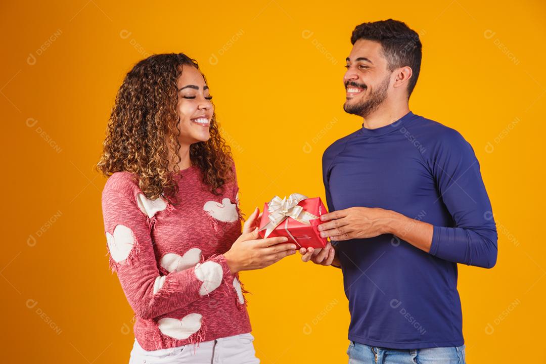 Retrato de um lindo casal em fundo amarelo com um presente