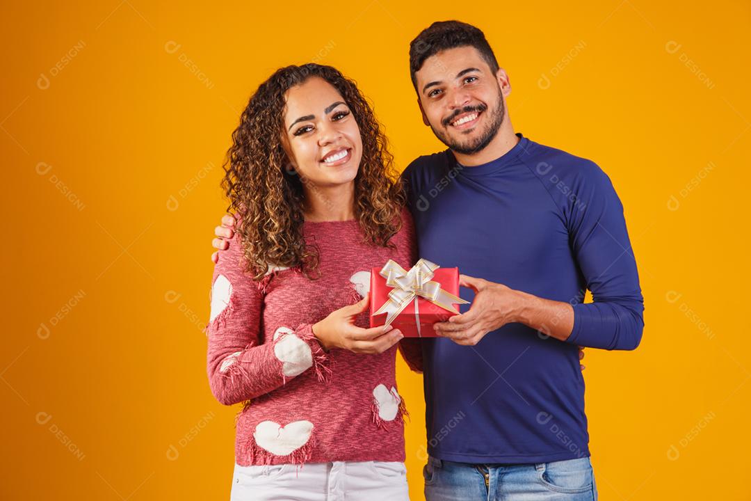 Retrato de um lindo casal em fundo amarelo com um presente