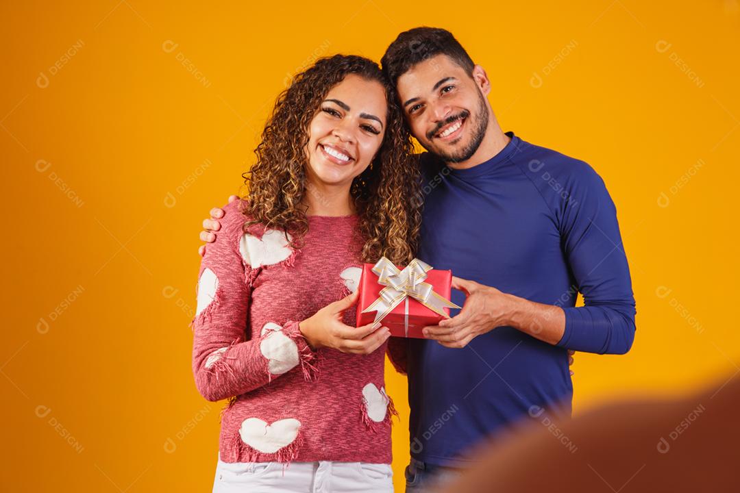 Retrato de um lindo casal em fundo amarelo com um presente