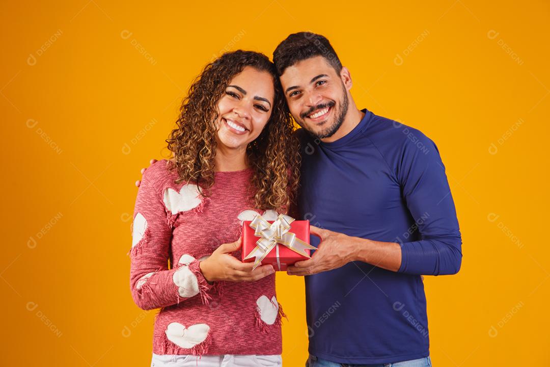 Retrato de um lindo casal em fundo amarelo com um presente