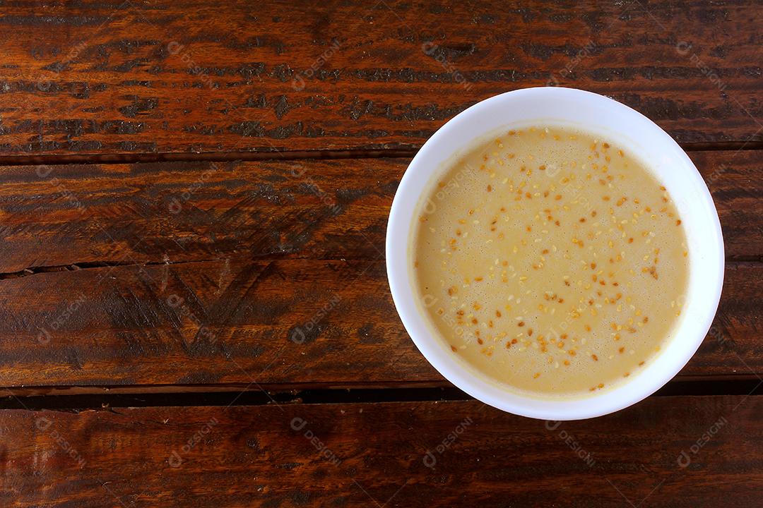 Tahine em tigela de cerâmica na mesa de madeira rústica - creme ou pasta feita de sementes de gergelim