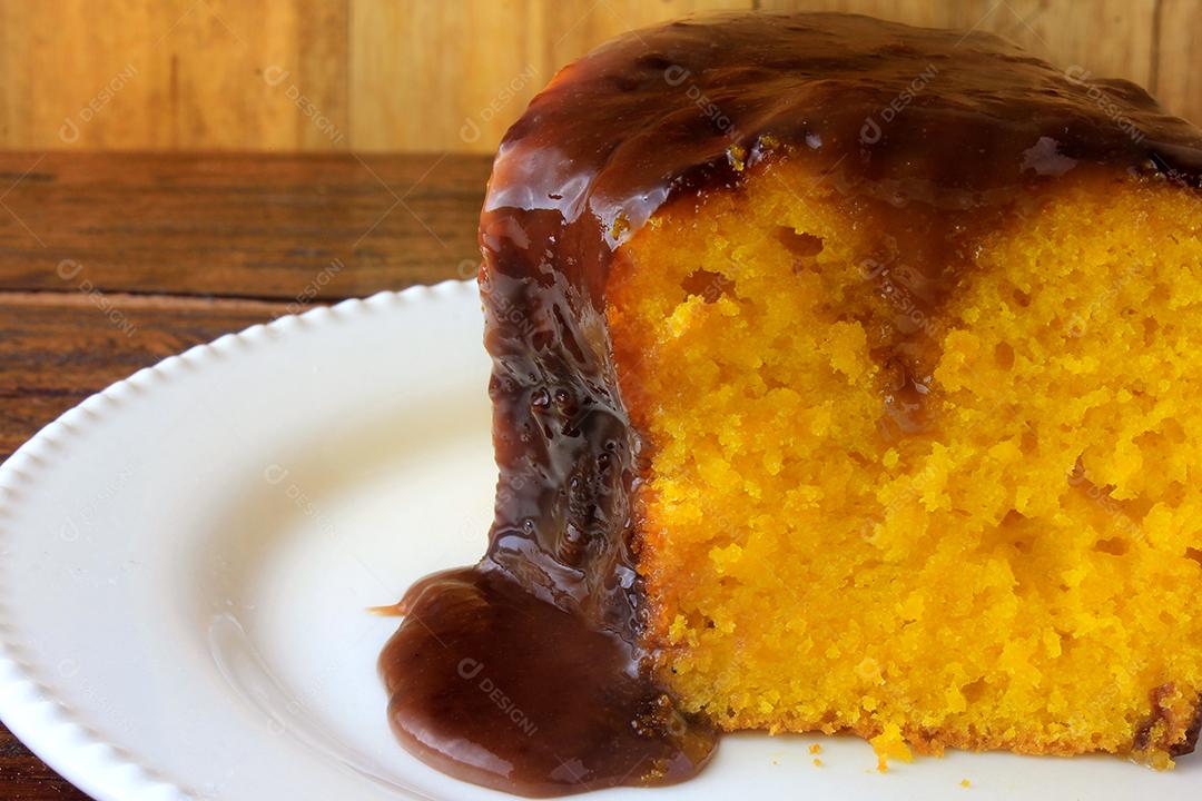 fatia de bolo de cenoura com cobertura de chocolate na placa cerâmica branca na mesa de madeira rústica