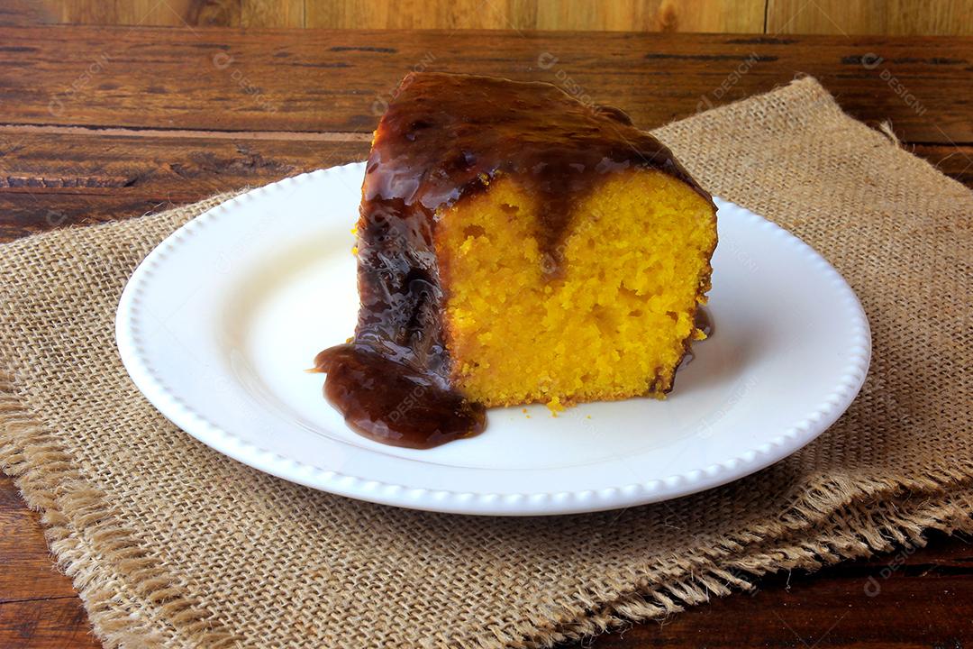 fatia de bolo de cenoura com cobertura de chocolate na placa cerâmica branca na mesa de madeira rústica