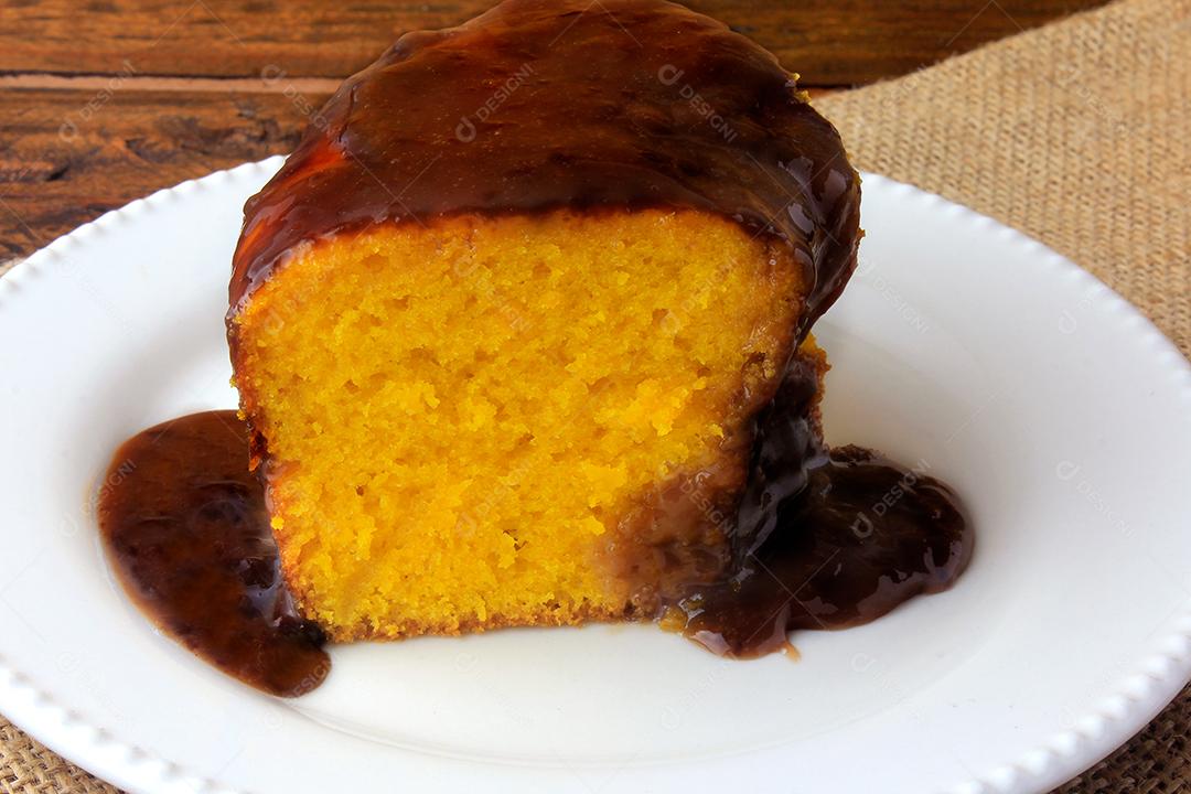 fatia de bolo de cenoura com cobertura de chocolate na placa cerâmica branca na mesa de madeira rústica