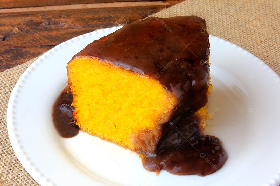 fatia de bolo de cenoura com cobertura de chocolate na placa cerâmica branca na mesa de madeira rústica