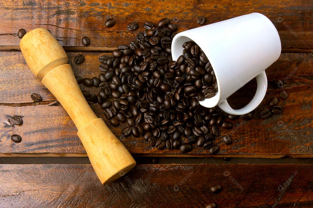 caneca branca com grãos de café torrados e frescos derramados sobre a mesa de madeira rústica