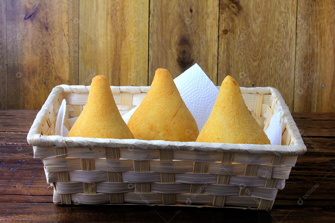 Coxinha na cesta, petiscos da cozinha tradicional brasileira recheados com frango, isolados na mesa de madeira