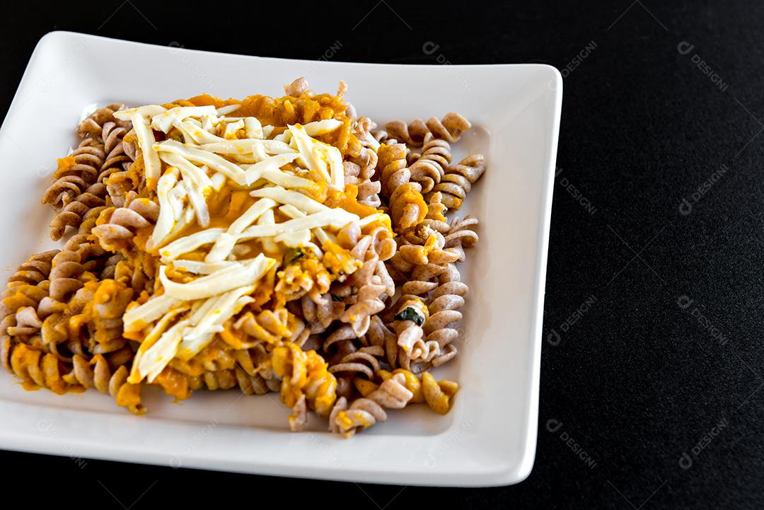 Macarrão Fusilli com molho de abóbora e queijo colonial, prato de comida caseira em fundo preto
