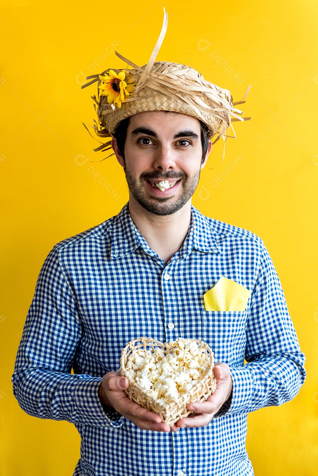 Feliz homem brasileiro com chapéu de palha na festa de junho, segurando uma cesta de pipoca